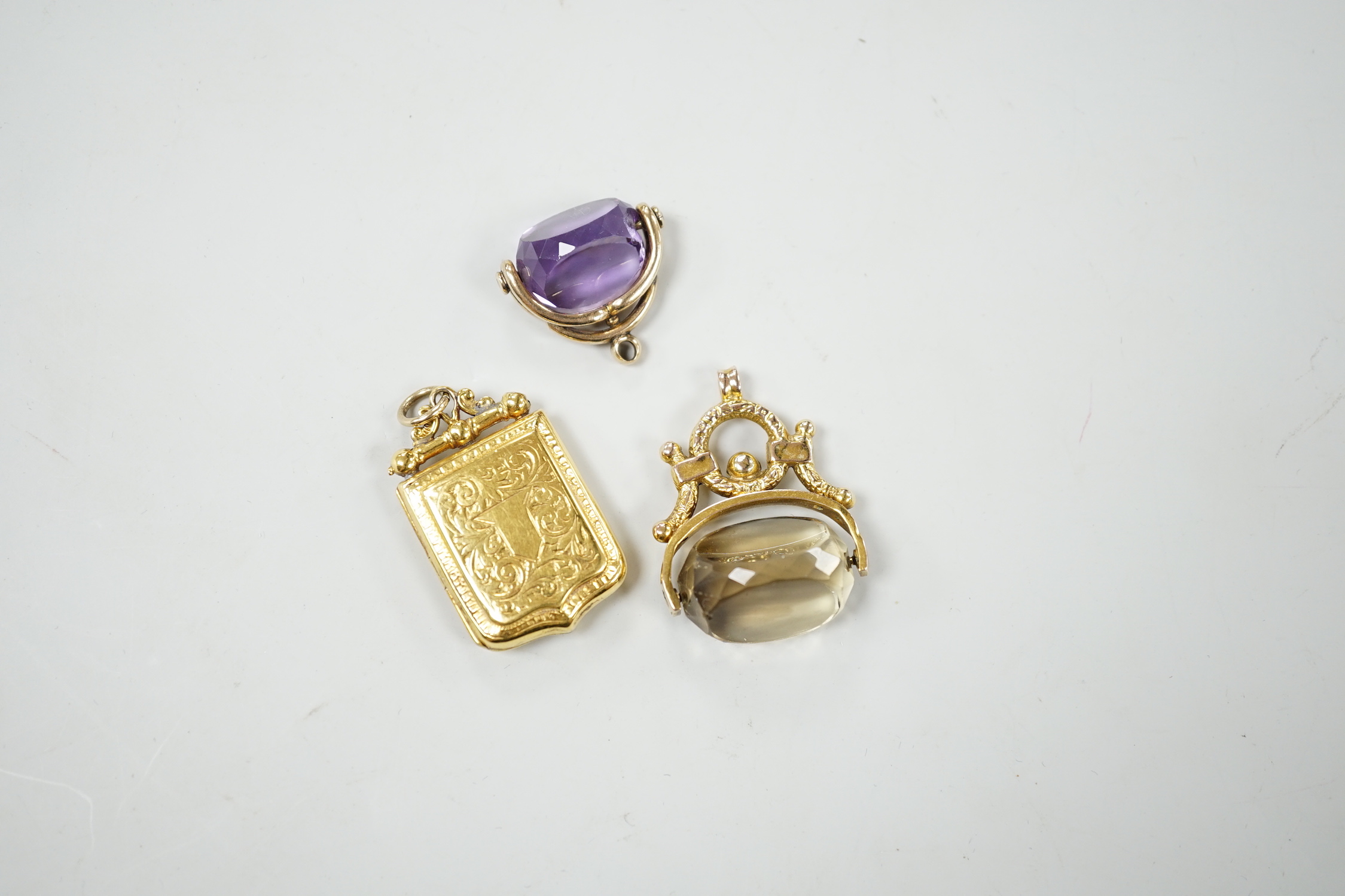 A Victorian engraved yellow metal shield shaped locket, 33mm and two yellow metal and gem set spinning fobs.